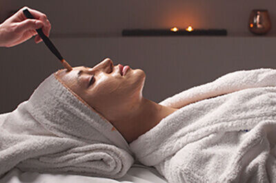 Spa therapy for young woman receiving facial mask at beauty salon. Beautician does face mask.